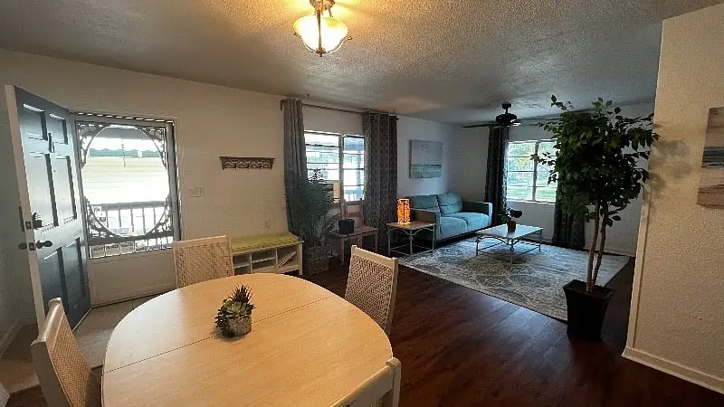 Oval dining table in the foreground with the living area and its windows behind