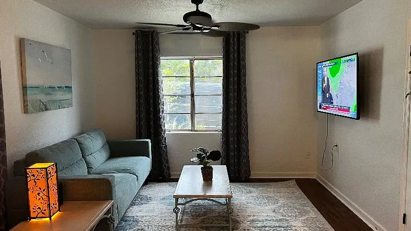 Living room under a ceiling fan, with the television on the wall beside a window