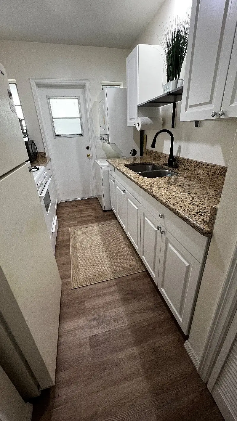 Galley kitchen with white cabinets, granite counters and a deep sink