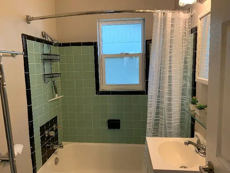 Bathroom with a green-tiled tub and shower beneath a frosted window