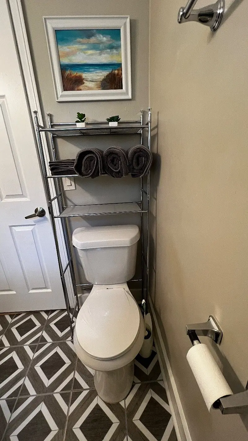 Bathroom with a toilet and a shelving rack holding rolled towels
