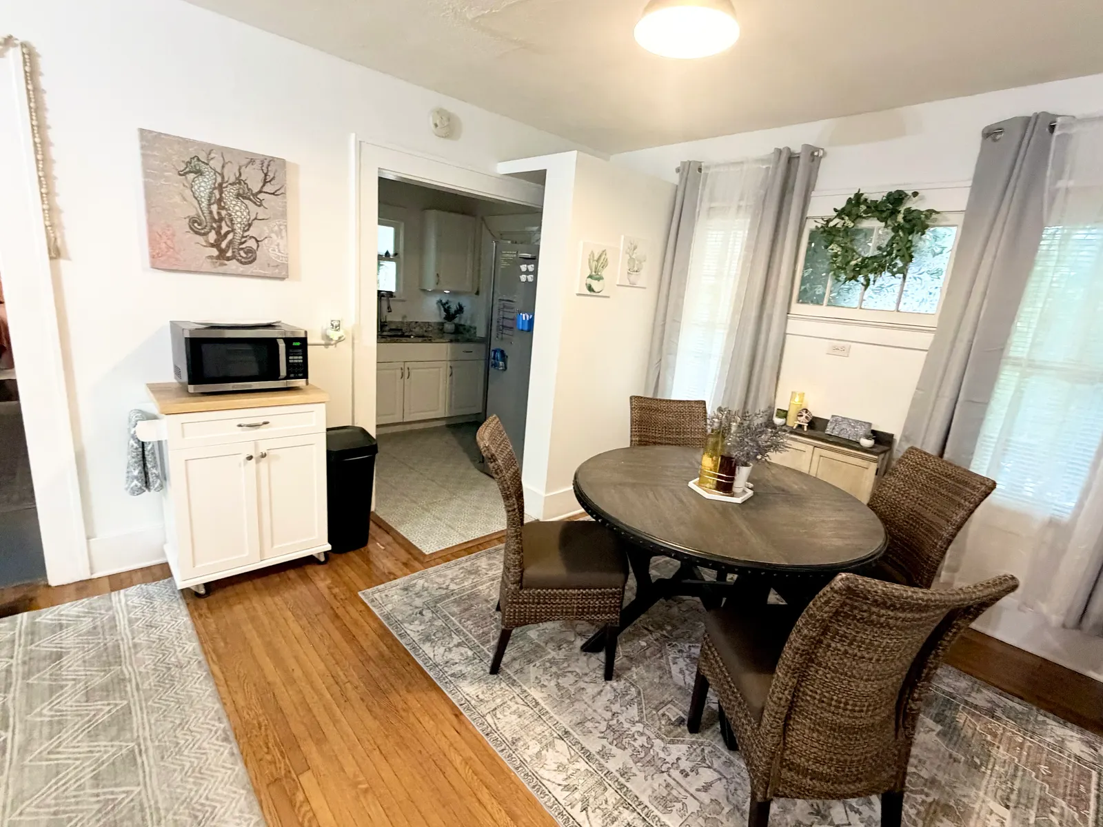 Dining area looking through an open doorway into the kitchen, with a microwave on a rolling cart beside the door and a refrigerator visible inside