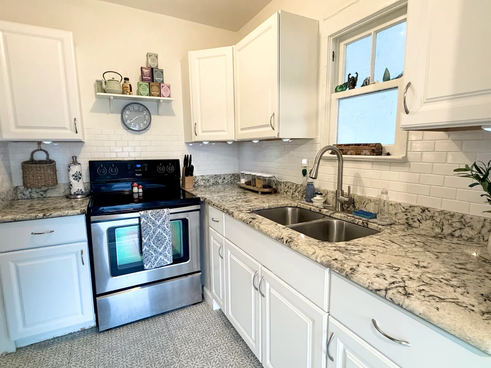 Kitchen from the far end, showing a stainless electric range and oven, granite counter running into the corner, and the two-bowl sink under the window
