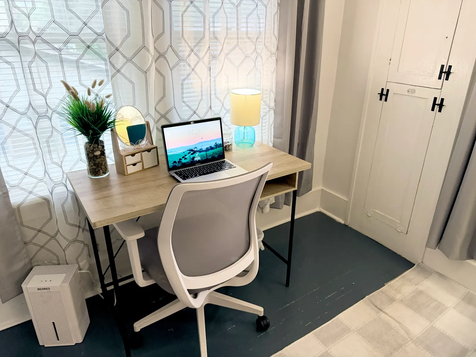 Desk and office chair in the main bedroom, set in front of a curtained window beside a tall built-in cupboard